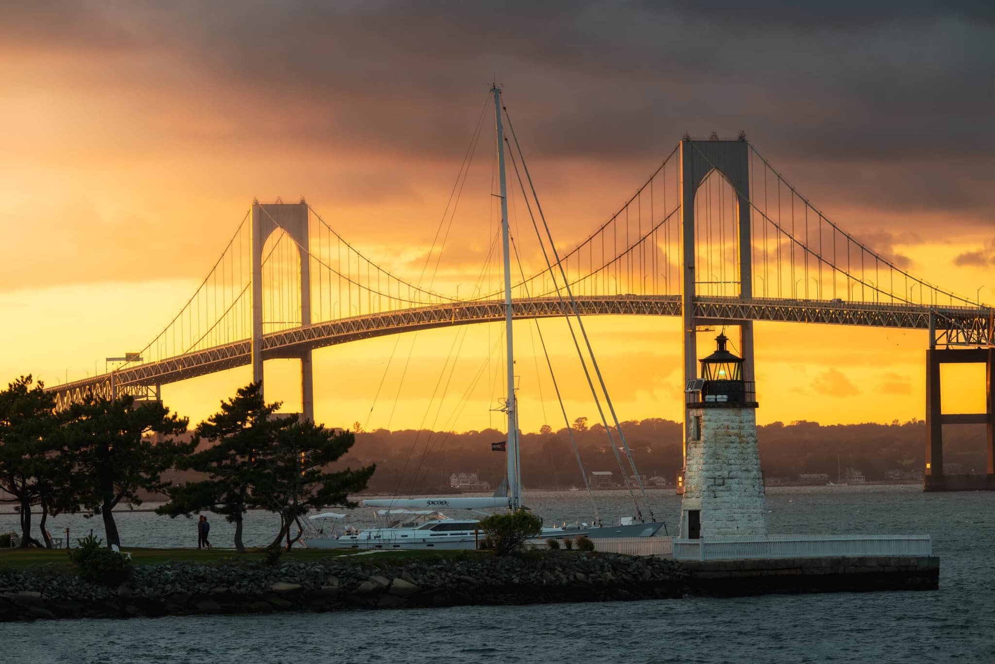 Newport Bridge and a lighthouse at sunset with a sailboat passing, Rhode Island