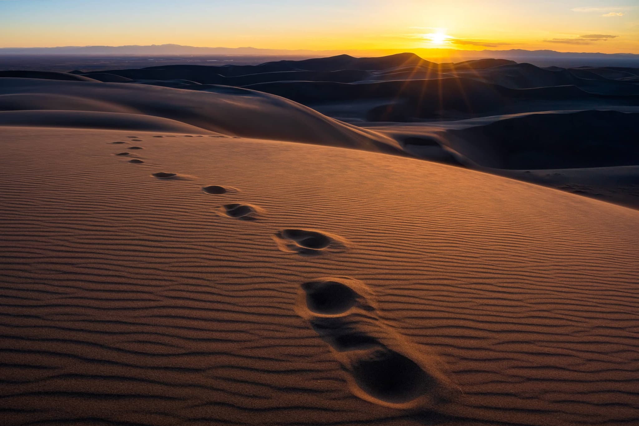 Footprints across sand dunes at sunset