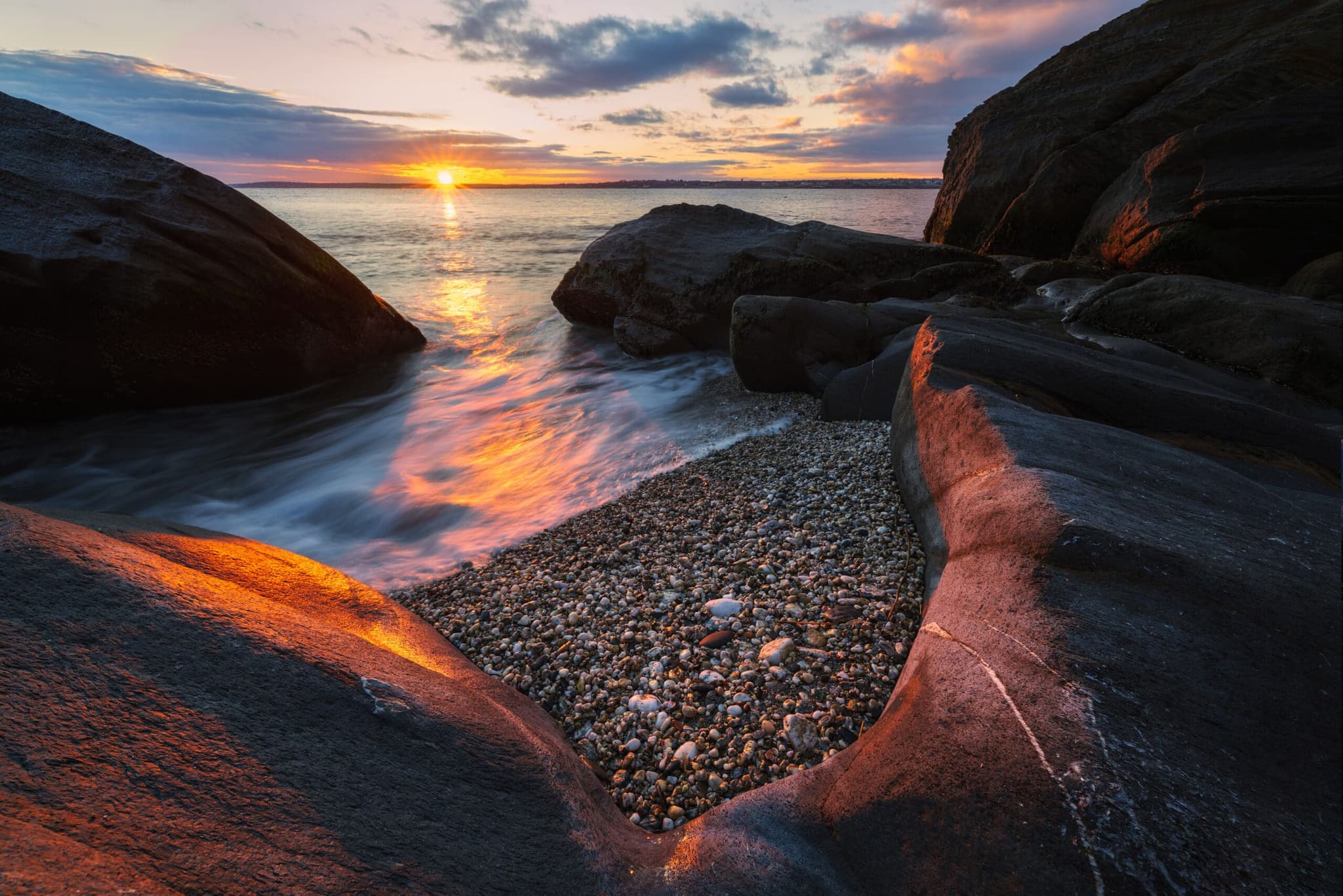 Low sun between dark rocks at Beavertail